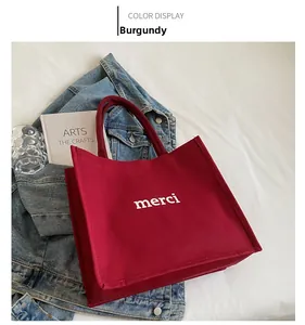 Detail of burgundy canvas tote bag with white merci print on a soft white background