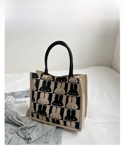 Close-up of canvas tote bag with rabbit checkerboard pattern and rope handles on white bedding