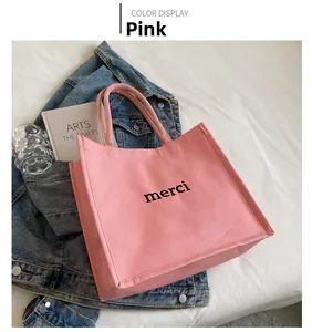 Detail view of pink canvas tote bag with black merci lettering and durable handles