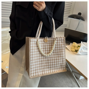 Close-up of houndstooth tote bag featuring pearl chain strap and wooden button closure
