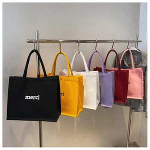 Row of colorful canvas tote bags with merci lettering hanging on metal hangers