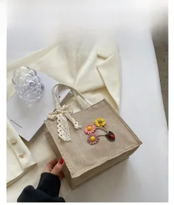 Linen tote bag detail with floral daisy embroidery, lace bow, and secure zipper closure
