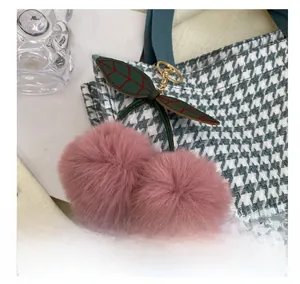 Close-up of a pink plush cherry bag charm with golden keychain on houndstooth canvas tote