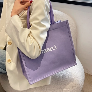 Minimalist purple canvas tote bag with white merci text shown on a female model shoulder