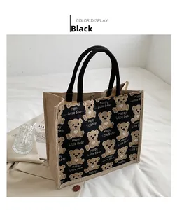 Detail of black canvas tote bag with bear print and sturdy woven handles on white surface