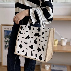Large cow print canvas tote bag with braided rope handles shown on a model