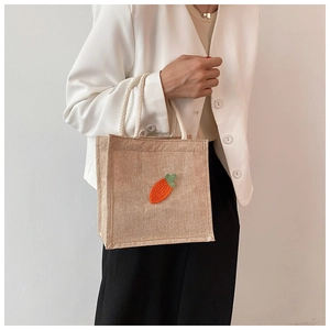 Detailed embroidery of a carrot on a natural jute tote bag with soft braided rope handles