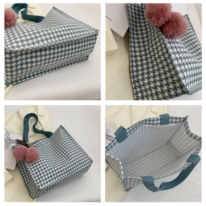 Detail of blue houndstooth tote bag with pink pom-pom charms and spacious interior