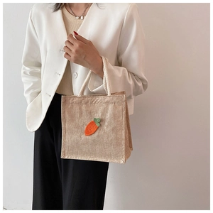 Detailed view of jute tote bag with carrot embroidery held by a model in casual attire