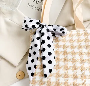 Close-up of a black and white polka dot silk scarf tied in a bow on a woven handbag handle