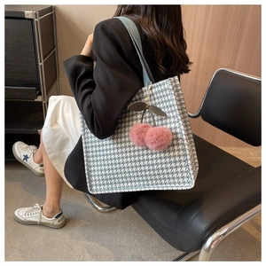 Detail of houndstooth tote bag featuring a light blue strap and pink cherry pendant