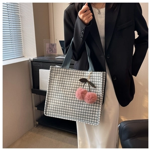 Detail of grey houndstooth tote bag with blue handles and pink cherry charm accessory