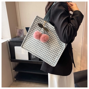 Detail of houndstooth tote bag featuring a plush cherry charm and dark green handles