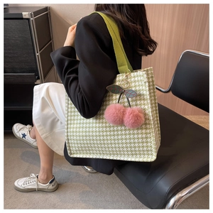 Detail of green houndstooth tote bag featuring a cute pink plush cherry charm accessory