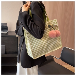 Detail of green houndstooth tote bag featuring a cute pink cherry plush charm accessory