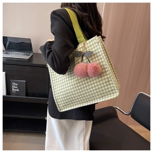 Detailed view of green houndstooth tote bag featuring a pink cherry plush charm accessory