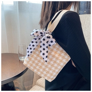 Detail view of woven straw handbag with yellow patterns and polka dot ribbon bow decoration