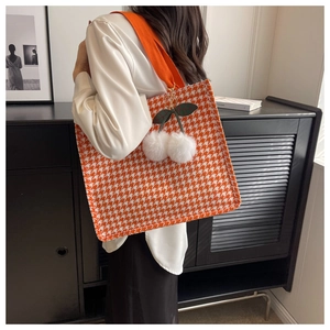 Detail of orange houndstooth tote bag featuring a plush cherry charm and wide strap