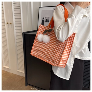 Detail of orange houndstooth tote bag featuring a decorative plush cherry charm on shoulder