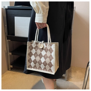 Detail of argyle canvas tote bag featuring woven rope handles and a wooden button closure