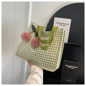 Detailed view of green houndstooth tote bag featuring cute pink cherry pompom charms