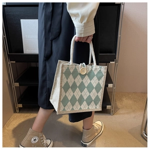 Detail of green argyle canvas bag with rope handles and button closure carried by model