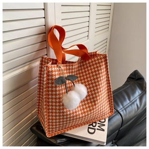 Detail of orange houndstooth tote bag featuring a cute plush cherry charm and woven straps