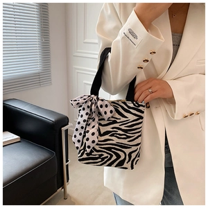 Detail view of zebra print canvas handbag with polka dot ribbon held by a model