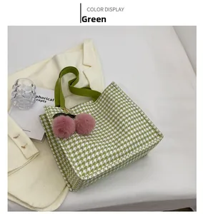 Detail shot of a green houndstooth tote bag with pink pompom charm and wide strap