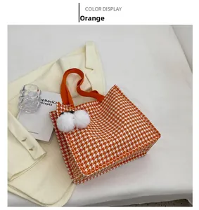 Detail view of orange houndstooth tote bag with white faux fur pom-poms and fabric handles
