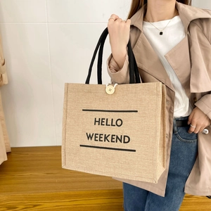 Detail of jute tote bag with HELLO WEEKEND print and wooden button closure