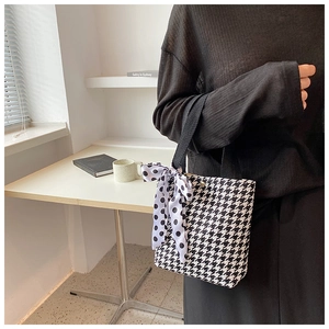 Detail of houndstooth canvas bucket bag with polka dot ribbon and woven strap