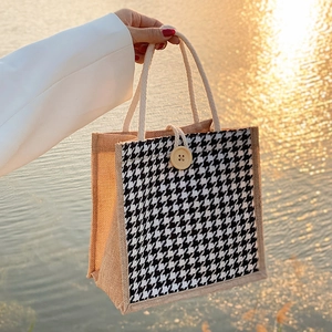 Linen tote bag with houndstooth panel and wooden button held near sunset water