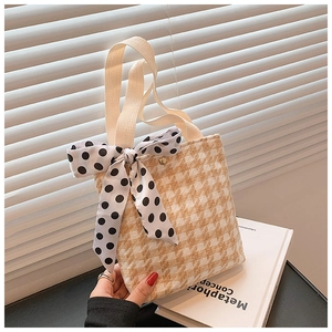 Detail of yellow houndstooth handbag featuring a polka dot ribbon and magnetic gold clasp