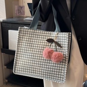 Blue houndstooth tote bag with pink cherry charm shown in a modern urban lifestyle setting