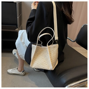 Detail of geometric woven bucket bag featuring white leather trim and a wide shoulder strap