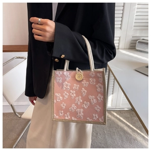 Detail of pink floral linen lunch bag featuring woven rope handles and wood button