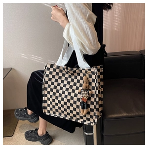 Detail of checkered canvas tote bag with a cute plush rabbit charm on a sofa