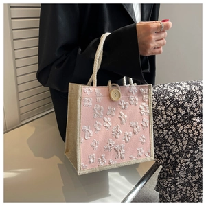 Detail view of a pink floral linen tote bag with white rope handles and vintage button