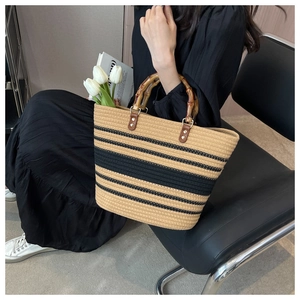 Detail of hand-woven straw tote bag with black stripes and unique bamboo top handles