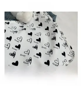 Close-up of white canvas tote bag with black heart prints, plush ball and neat stitching