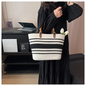 Close-up of woven tote bag featuring black and white stripes and natural bamboo handles