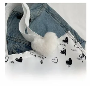 Detail of white canvas tote with heart patterns, featuring a plush heart charm and handles