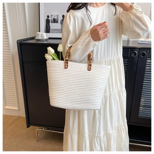 Detail of white woven tote bag featuring bamboo handles and brown leather accents