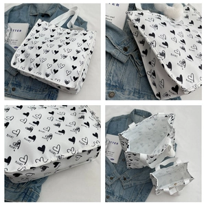 Detail view of large and small white canvas tote bags with black heart and nice print