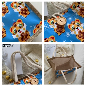 Detail view of cartoon tiger tote showing linen texture, rope handle, and wood button