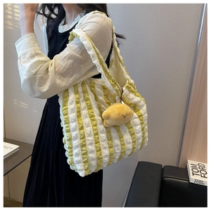 Detail view of yellow striped puffer bag with ruffled texture and plush charm on a model