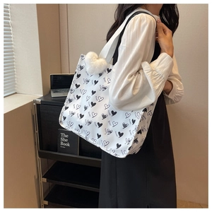 Large canvas tote bag with black heart prints and plush pendant shown on shoulder
