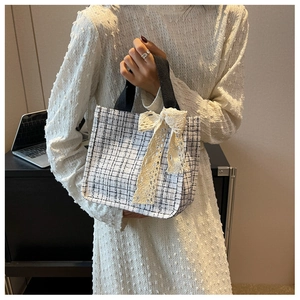 Detail of checkered tote bag featuring a large lace bow accent held by a model