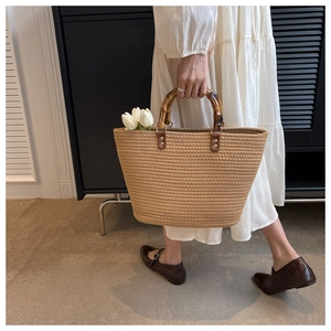 Close-up of woven straw tote bag featuring natural bamboo handles and leather buckles